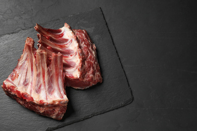 Photo of Raw ribs on black table, top view. Space for text