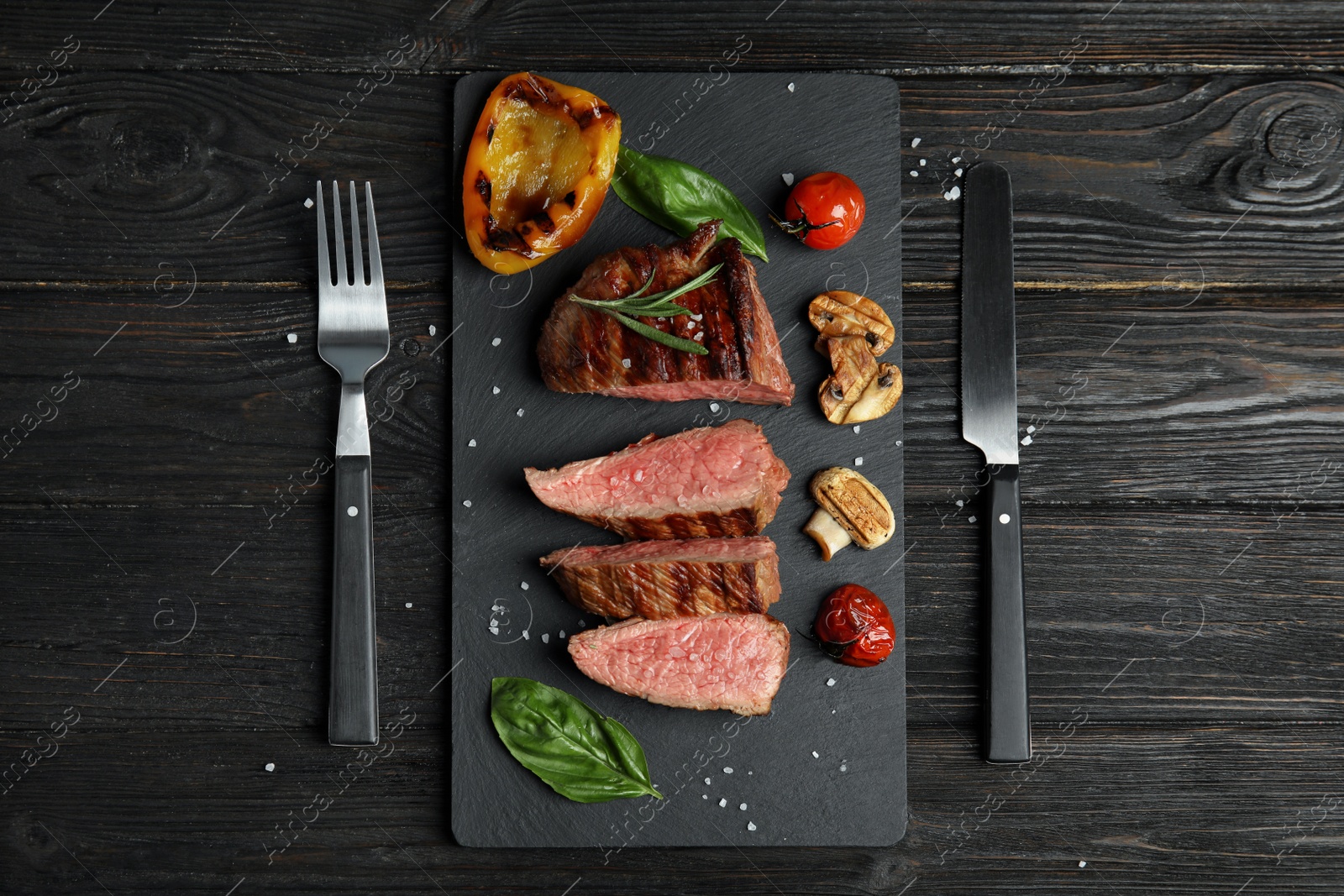 Photo of Flat lay composition with slices of grilled meat on black wooden table
