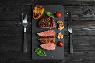 Photo of Flat lay composition with slices of grilled meat on black wooden table