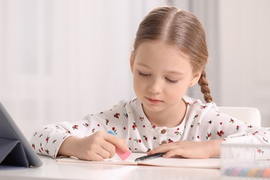 Photo of Girl using eraser at white desk indoors