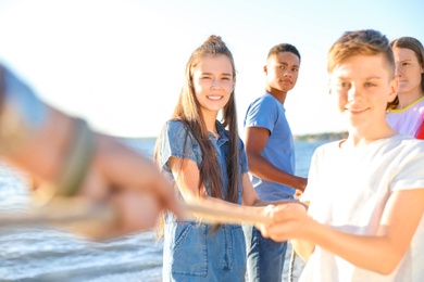 Group of children pulling rope during tug of war game on beach. Summer camp