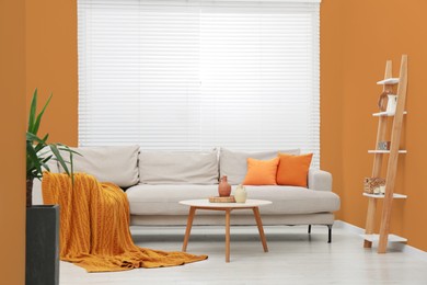 Photo of Stylish sofa and coffee table in room with orange walls. Interior design