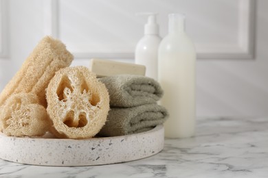 Photo of Loofah sponges, towels, soap and cosmetic products on white marble table, space for text