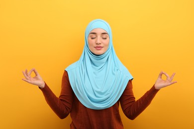 Muslim woman in hijab meditating on orange background