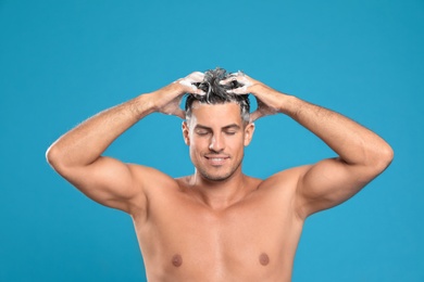 Photo of Handsome man washing hair on light blue background