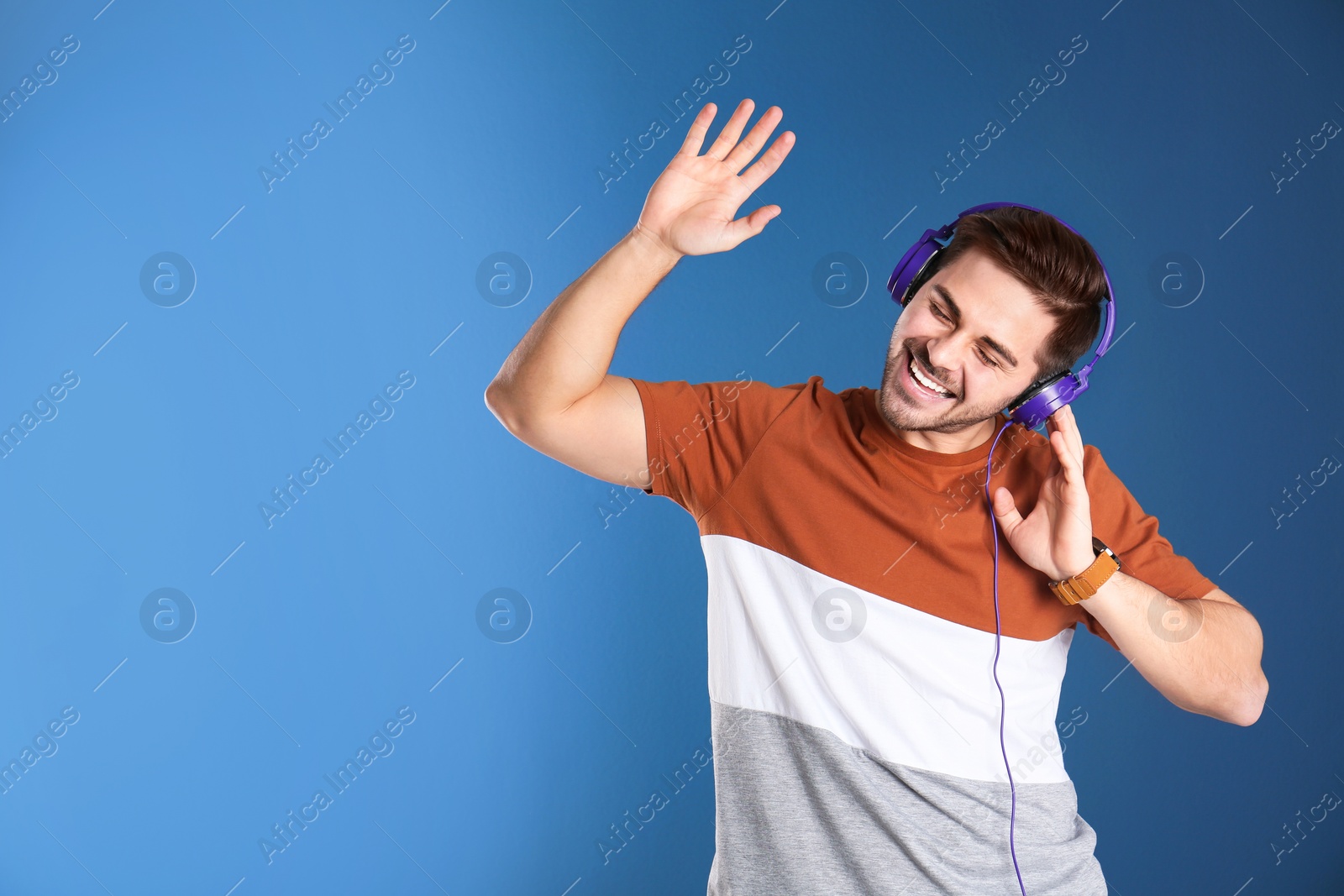 Photo of Handsome man with headphones enjoying music on color background. Space for text