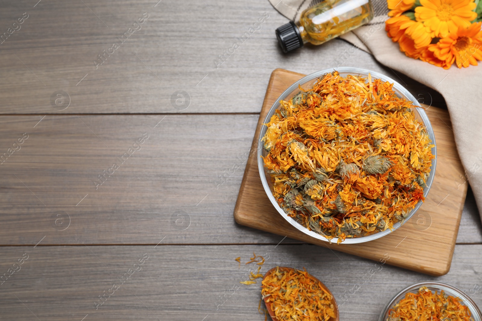 Photo of Dry calendula flowers and bottle with tincture on wooden table, flat lay. Space for text