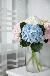 Beautiful hydrangea flowers in vase on white bedside table indoors