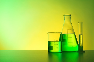 Chemistry laboratory glassware with samples on table against color background