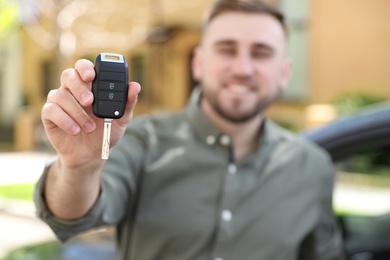 Image of Happy man with car key near his new auto outdoors, focus on hand
