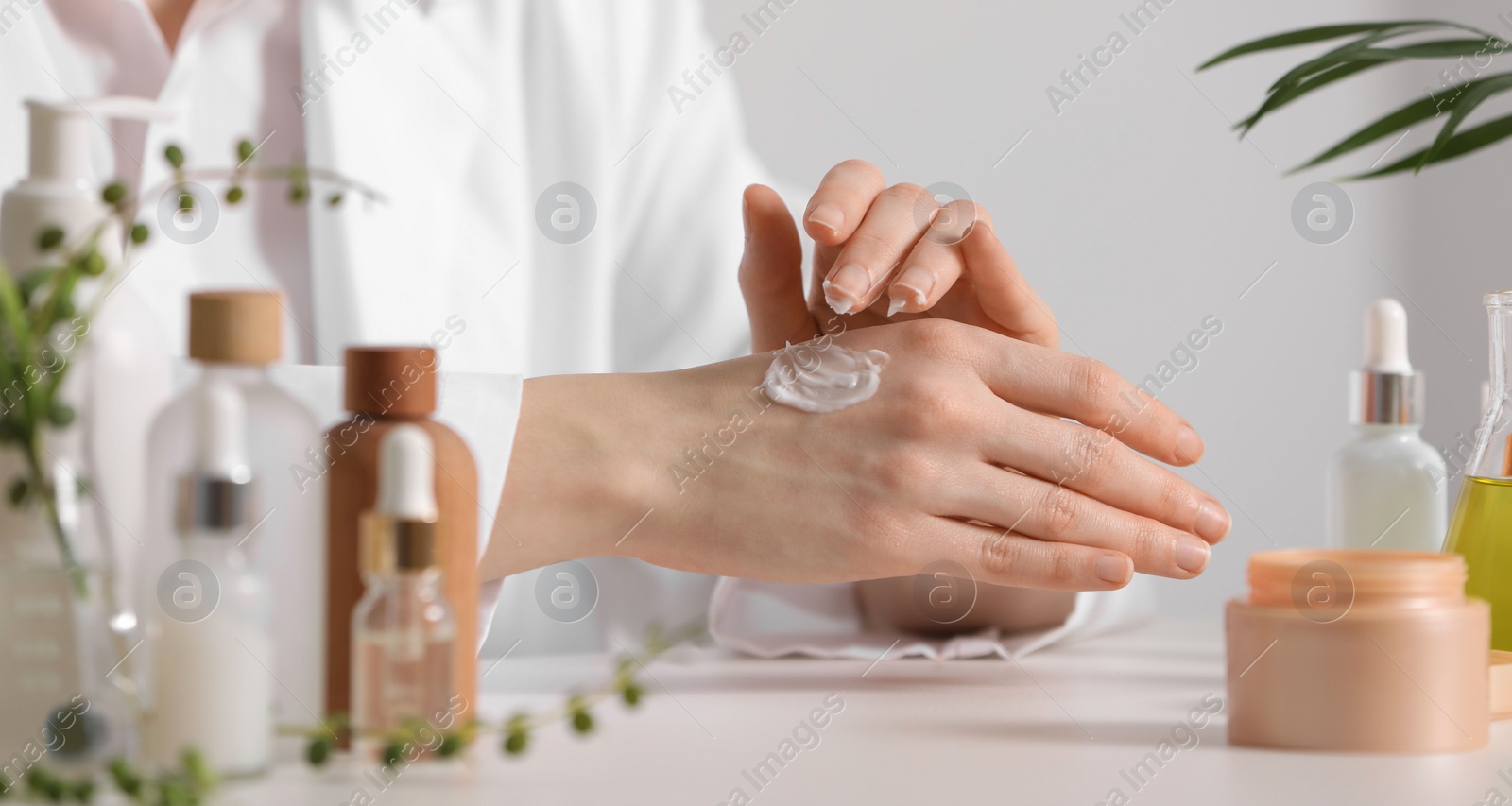 Photo of Dermatologist applying cream onto hand at white table indoors, selective focus. Testing cosmetic product