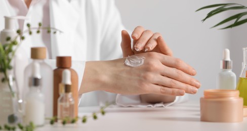 Dermatologist applying cream onto hand at white table indoors, selective focus. Testing cosmetic product