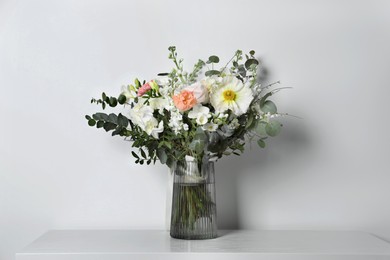 Photo of Bouquet of beautiful flowers in vase on table against white wall