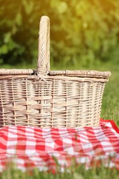 Picnic basket with checkered tablecloth on green grass outdoors