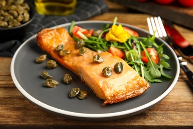 Photo of Tasty cooked salmon with capers and salad served on wooden table, closeup