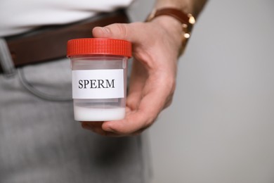 Donor holding container with sperm on beige background, closeup. Space for text