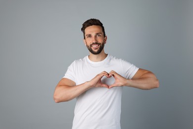 Photo of Happy man making heart with hands on grey background