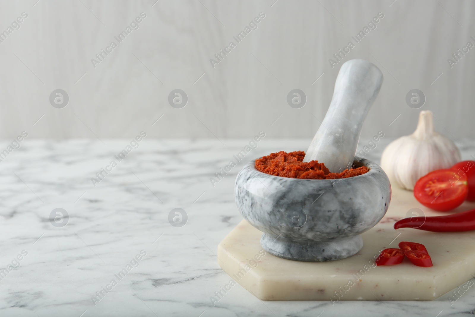 Photo of Red curry paste in mortar and ingredients on white marble table. Space for text