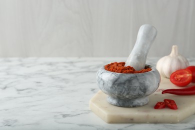 Photo of Red curry paste in mortar and ingredients on white marble table. Space for text