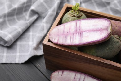 Photo of Purple and green daikon radishes in crate on black wooden table, closeup. Space for text
