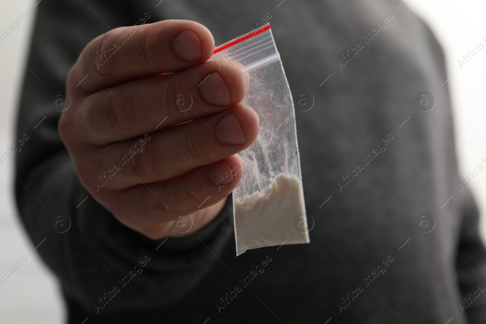 Photo of Drug addiction. Man with plastic bag of cocaine on light background, closeup