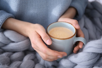 Woman with cup of coffee and knitted plaid, closeup