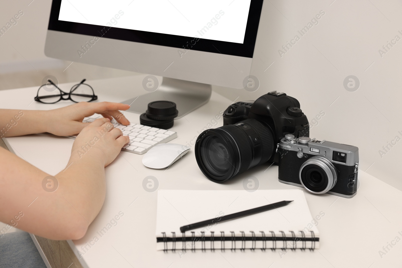 Photo of Photographer working on computer at white table with cameras indoors, closeup