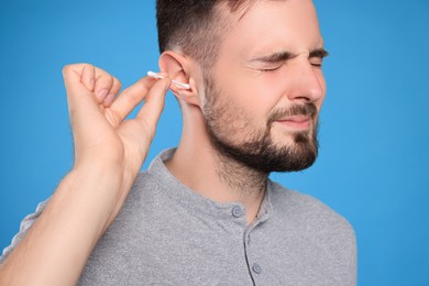 Young man cleaning ear with cotton swab on light blue background