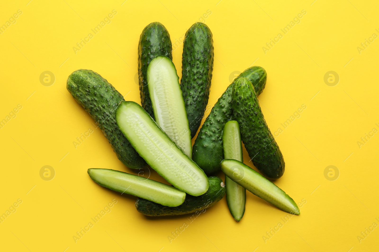 Photo of Whole and cut fresh cucumbers on yellow background, flat lay