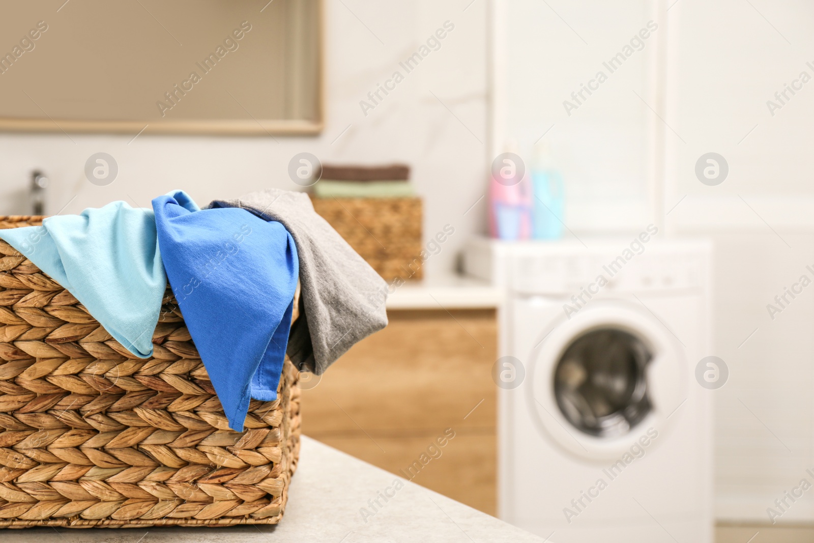 Photo of Wicker basket with laundry on countertop in bathroom, closeup. Space for text