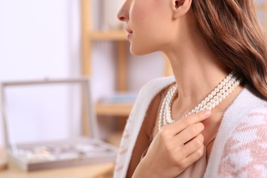 Young woman trying on elegant pearl necklace indoors, closeup. Space for text