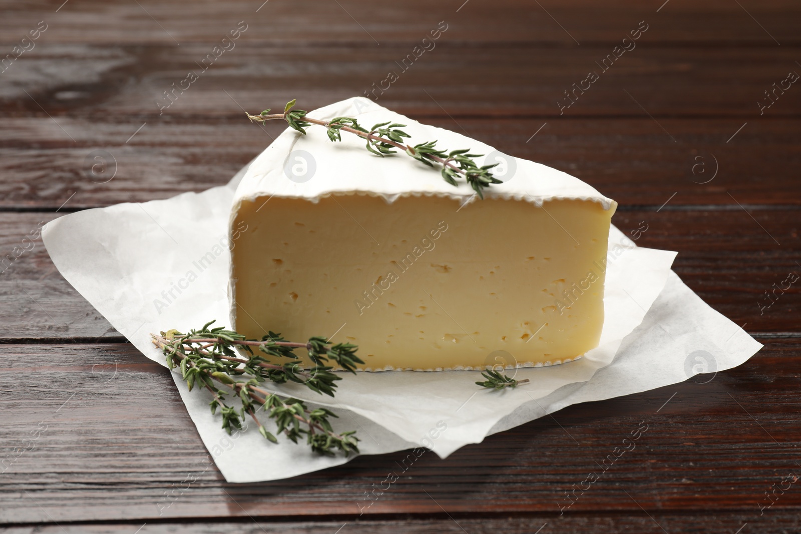 Photo of Piece of tasty camembert cheese and thyme on wooden table, closeup