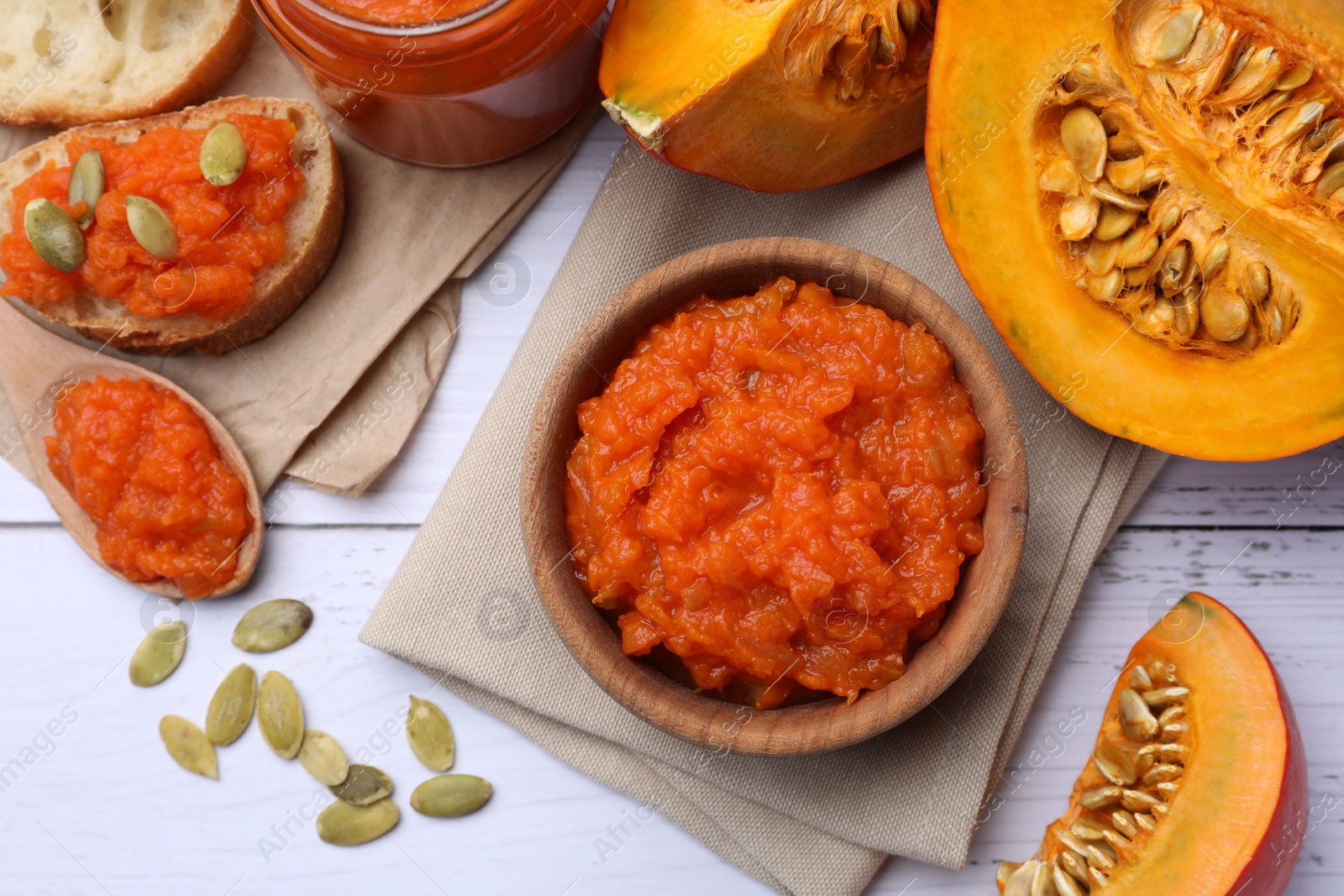 Photo of Delicious pumpkin jam and fresh pumpkin on white wooden table, flat lay