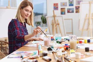 Photo of Beautiful woman painting at table in studio. Creative hobby