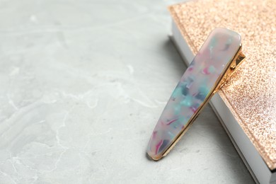 Stylish hair clip and book on grey marble table, space for text