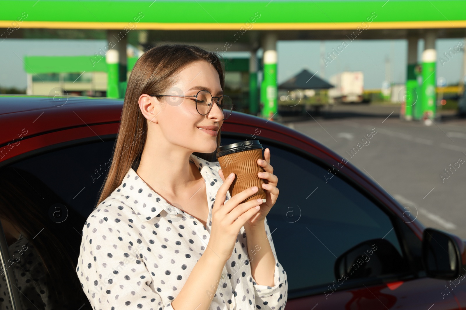 Photo of Beautiful young woman with coffee near car at gas station