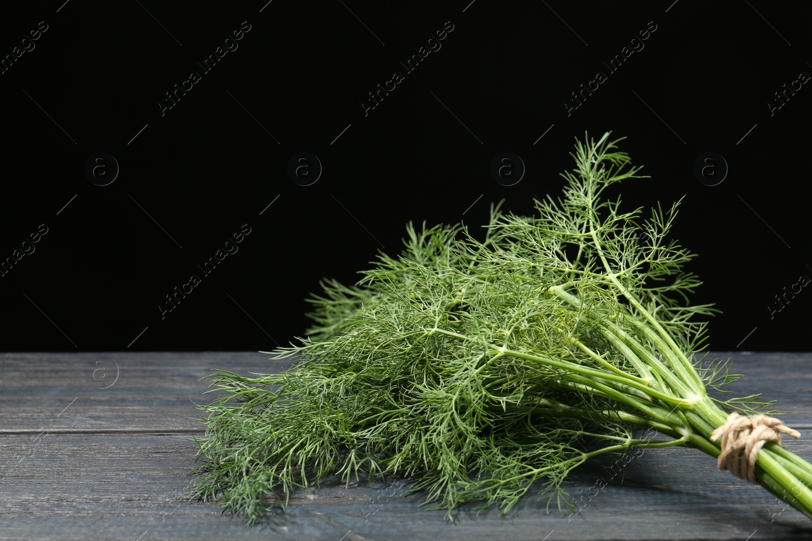 Photo of Bunch of fresh green dill on grey wooden table against black background. Space for text