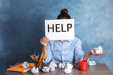 Woman holding card with word "HELP" at table in office