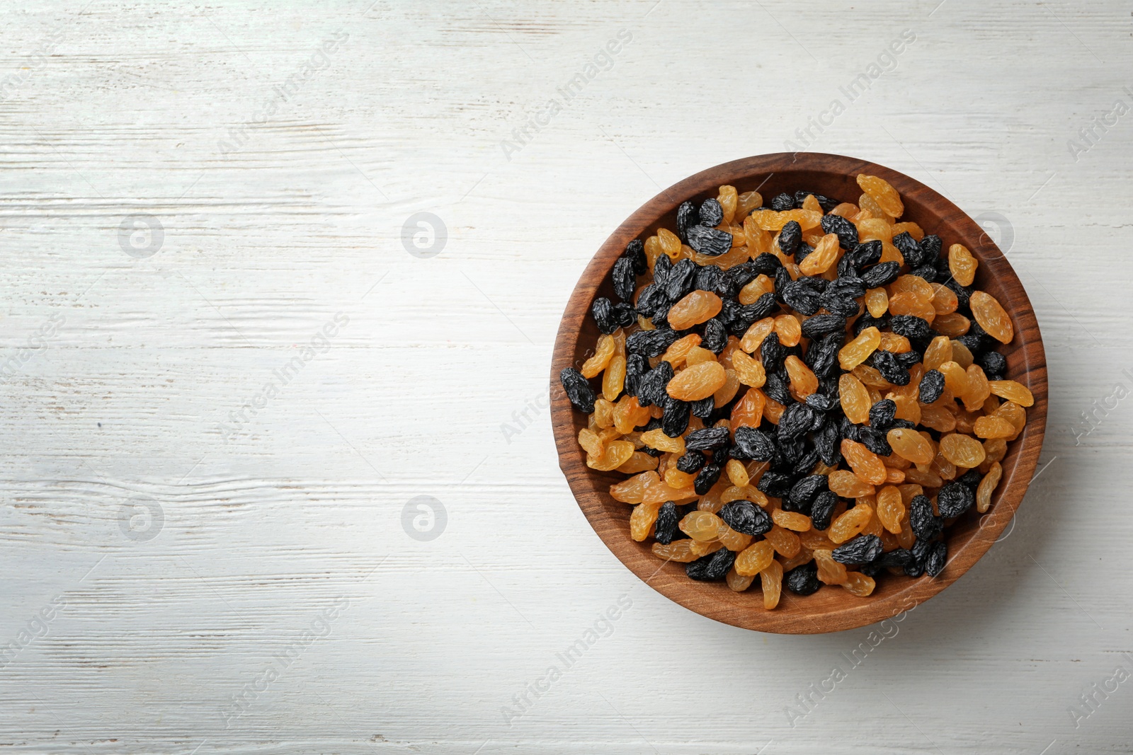 Photo of Bowl of raisins on wooden background, top view with space for text. Dried fruit as healthy snack