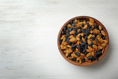 Photo of Bowl of raisins on wooden background, top view with space for text. Dried fruit as healthy snack