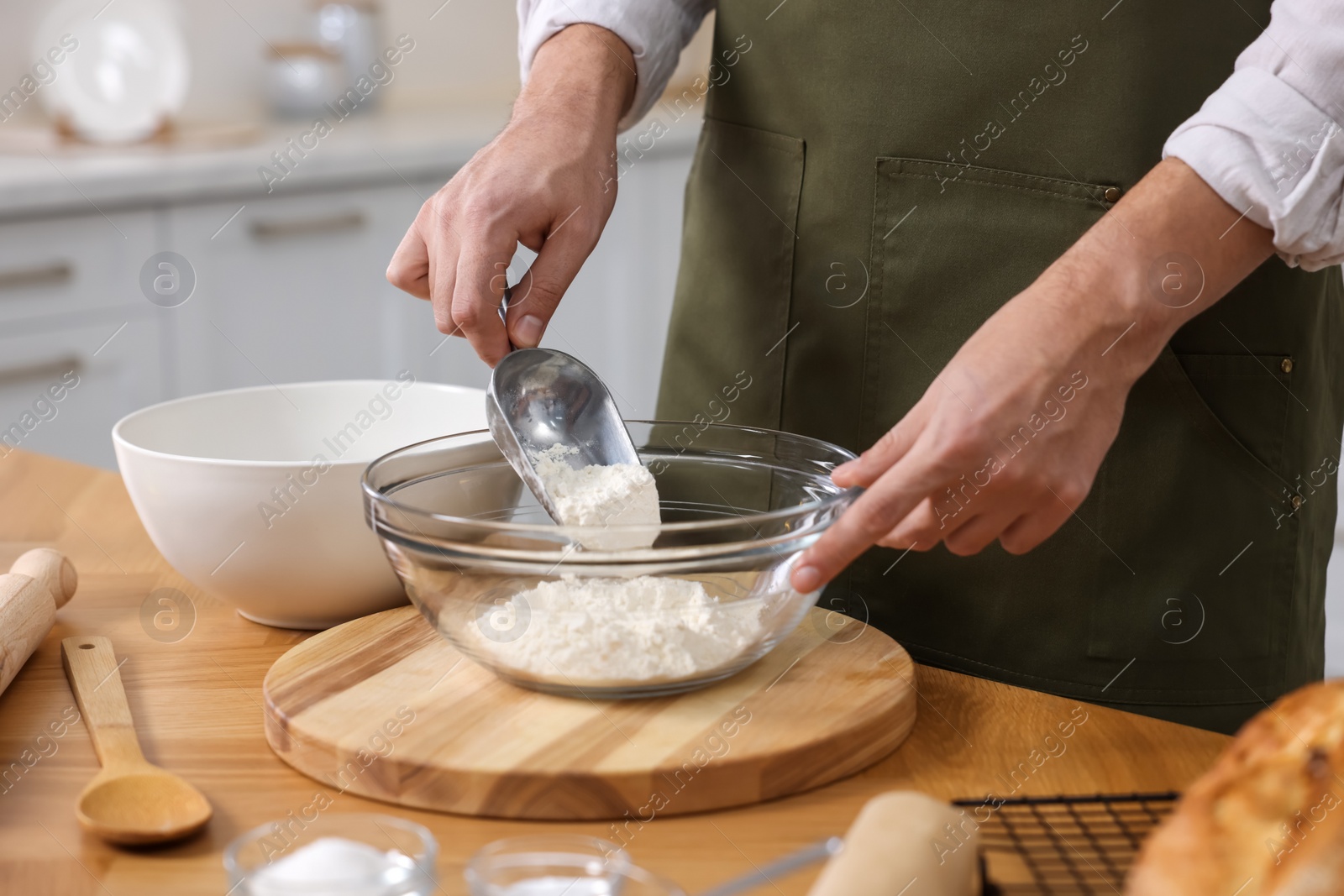 Photo of Making bread. Man putting flour into bowl at wooden table in kitchen, closeup