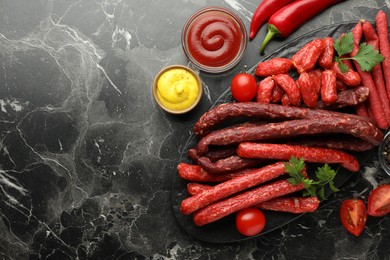 Photo of Thin dry smoked sausages served on black marble table, flat lay. Space for text