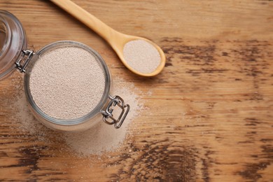 Glass jar and spoon with active dry yeast on wooden table, flat lay. Space for text