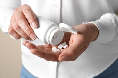 Photo of Woman pouring pills from bottle on beige background, closeup