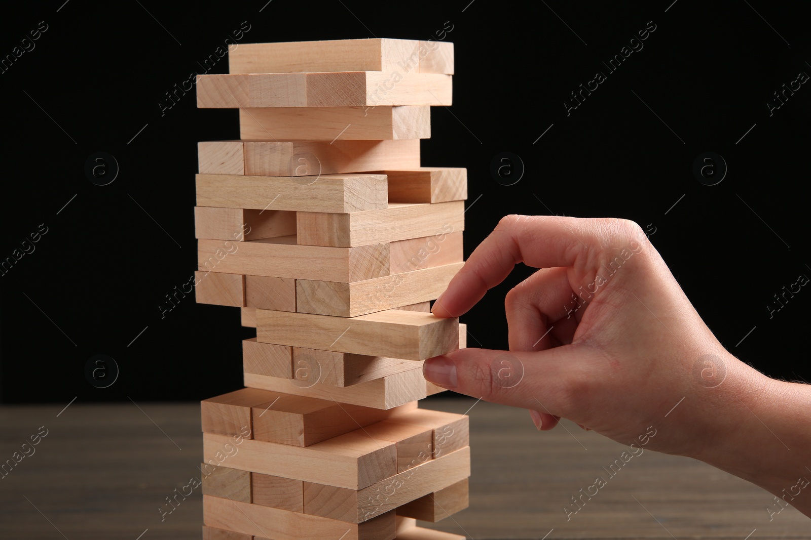 Photo of Woman playing Jenga at table against black background, closeup