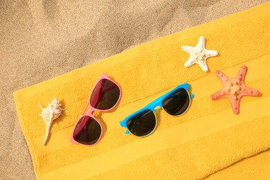 Stylish sunglasses, yellow towel, starfishes and seashell on sand, top view. Beach accessories