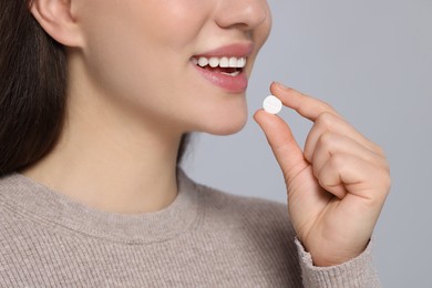 Woman taking pill on gray background, closeup