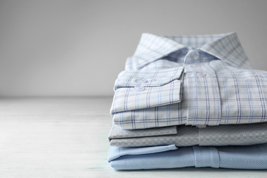 Photo of Stack of classic shirts on white wooden table. Space for text