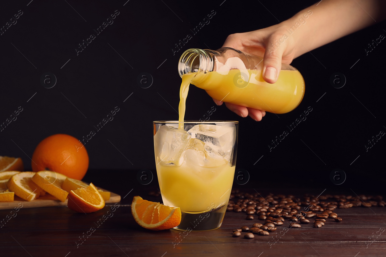 Photo of Woman pouring orange juice into glass with ice cubes at wooden table, closeup