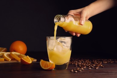Photo of Woman pouring orange juice into glass with ice cubes at wooden table, closeup